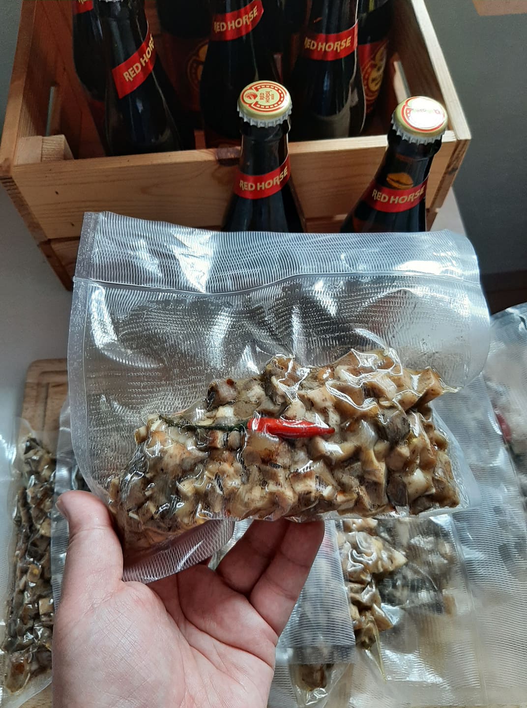 Hand holding a sealed pork sisig portion in front of bottled drinks