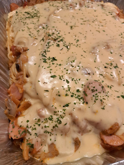 Sweet-style spaghetti tray with sliced sausage beneath a rich cheese topping