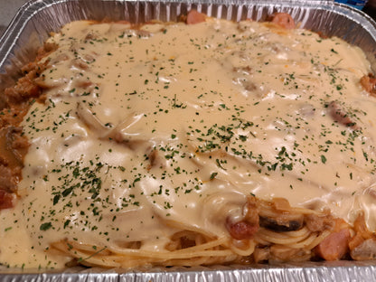 Sweet-style Filipino spaghetti in a foil tray with creamy cheese topping and herbs