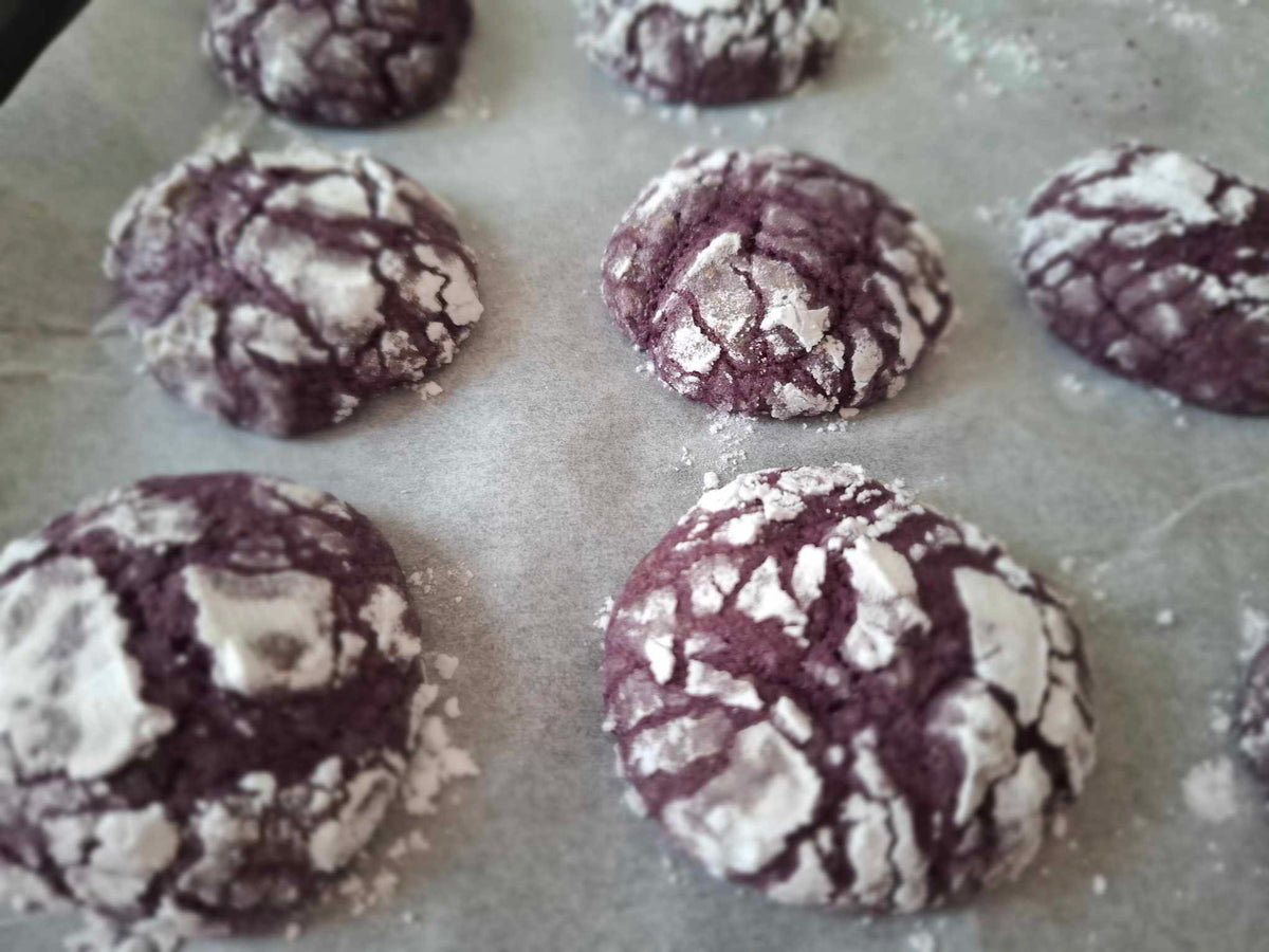 Freshly baked ube crinkle cookies cooling on baking paper