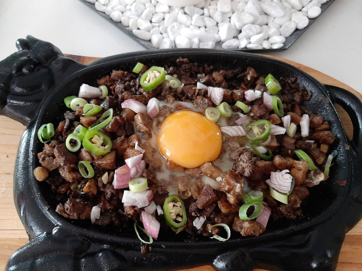Sizzling pork sisig topped with a raw egg yolk and green chillies