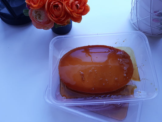 Whole leche flan with glossy caramel sauce in a clear container