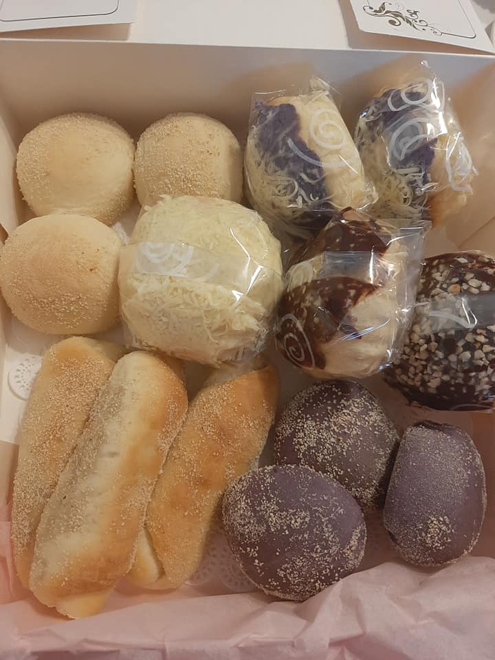 Assorted Filipino bread box with pale rolls, ube buns and wrapped pastries