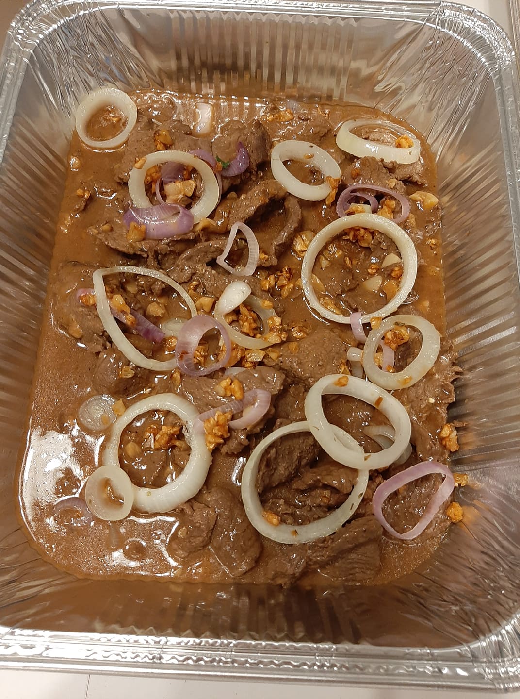 Foil tray of Bistek Tagalog with beef slices, onions and rich sauce