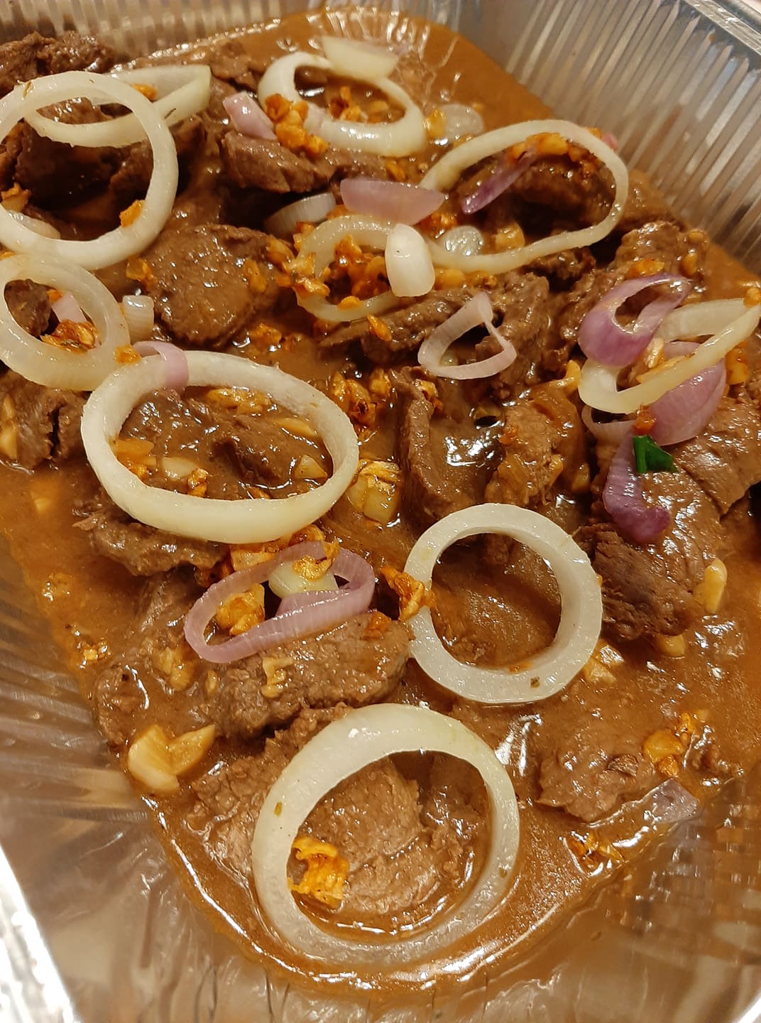 Close-up of tender Bistek Tagalog beef with white and red onion rings