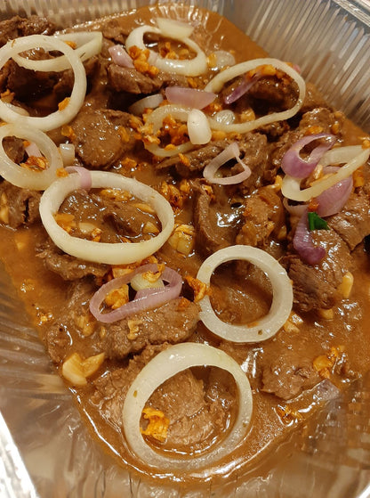Close-up of tender Bistek Tagalog beef with white and red onion rings