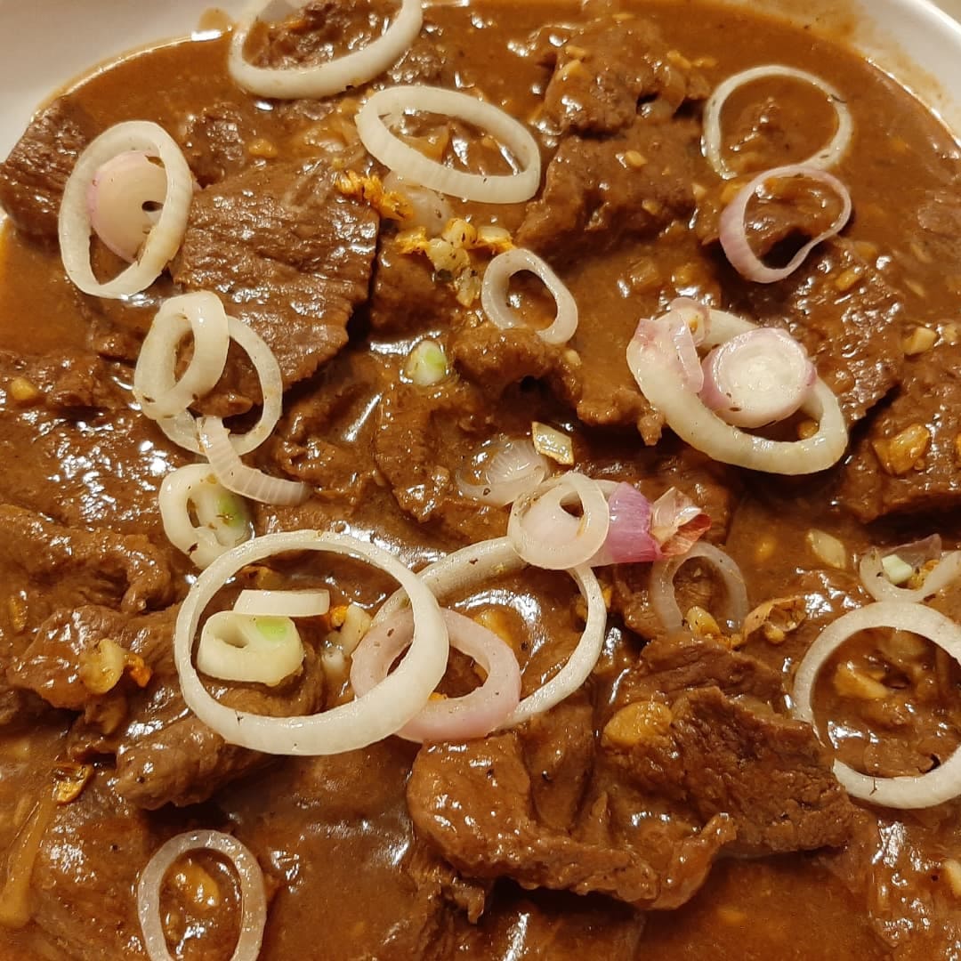 Bistek Tagalog served in a deep tray with fresh onion garnish