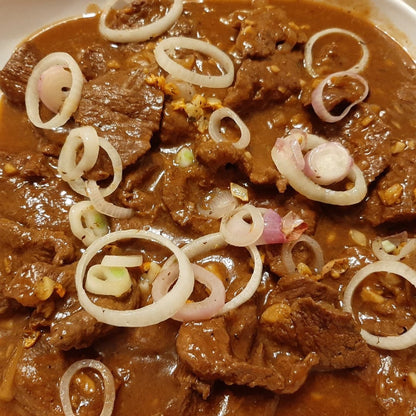 Bistek Tagalog served in a deep tray with fresh onion garnish