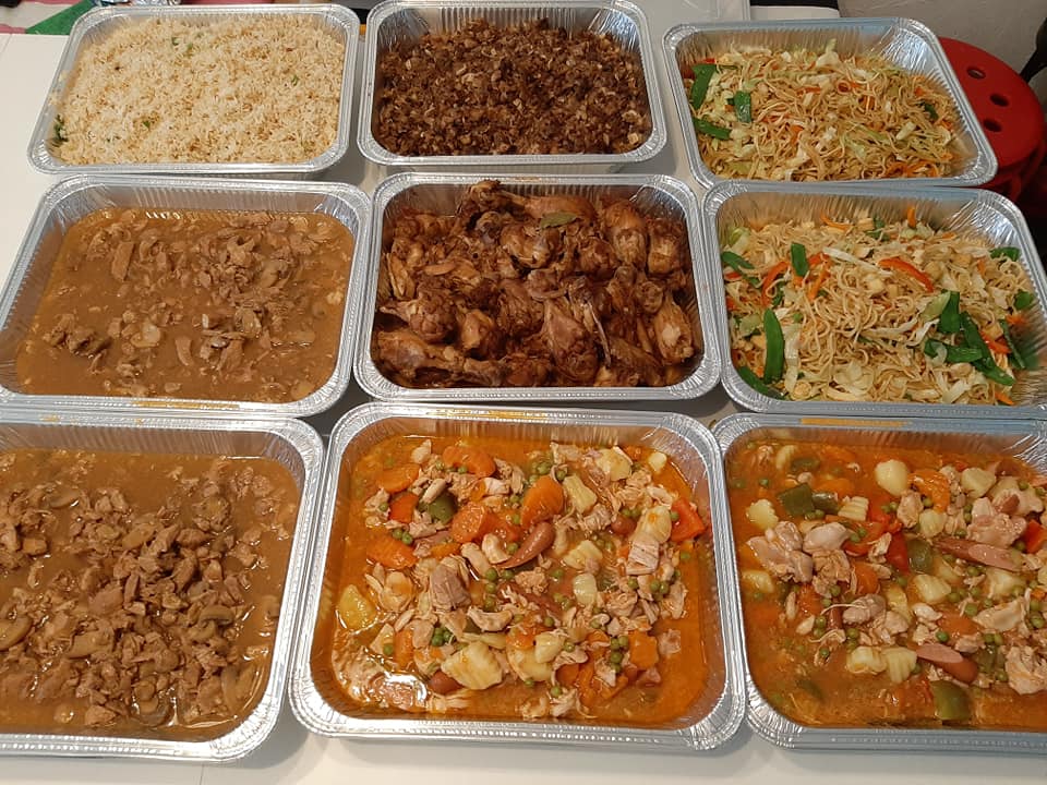 Catering spread featuring chicken adobo with rice, noodles and other dishes