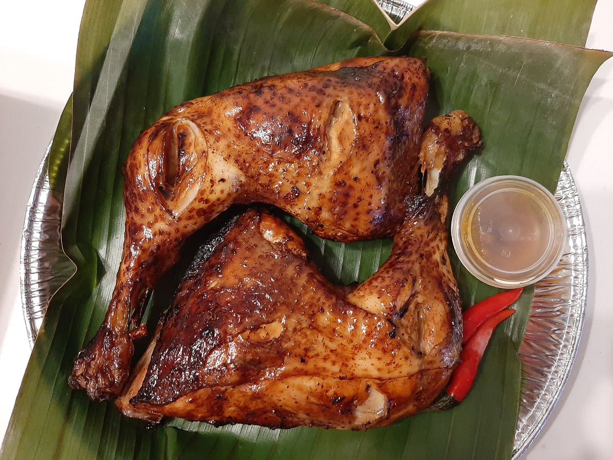Two baked chicken inasal thighs on banana leaves with dipping sauce and chillies