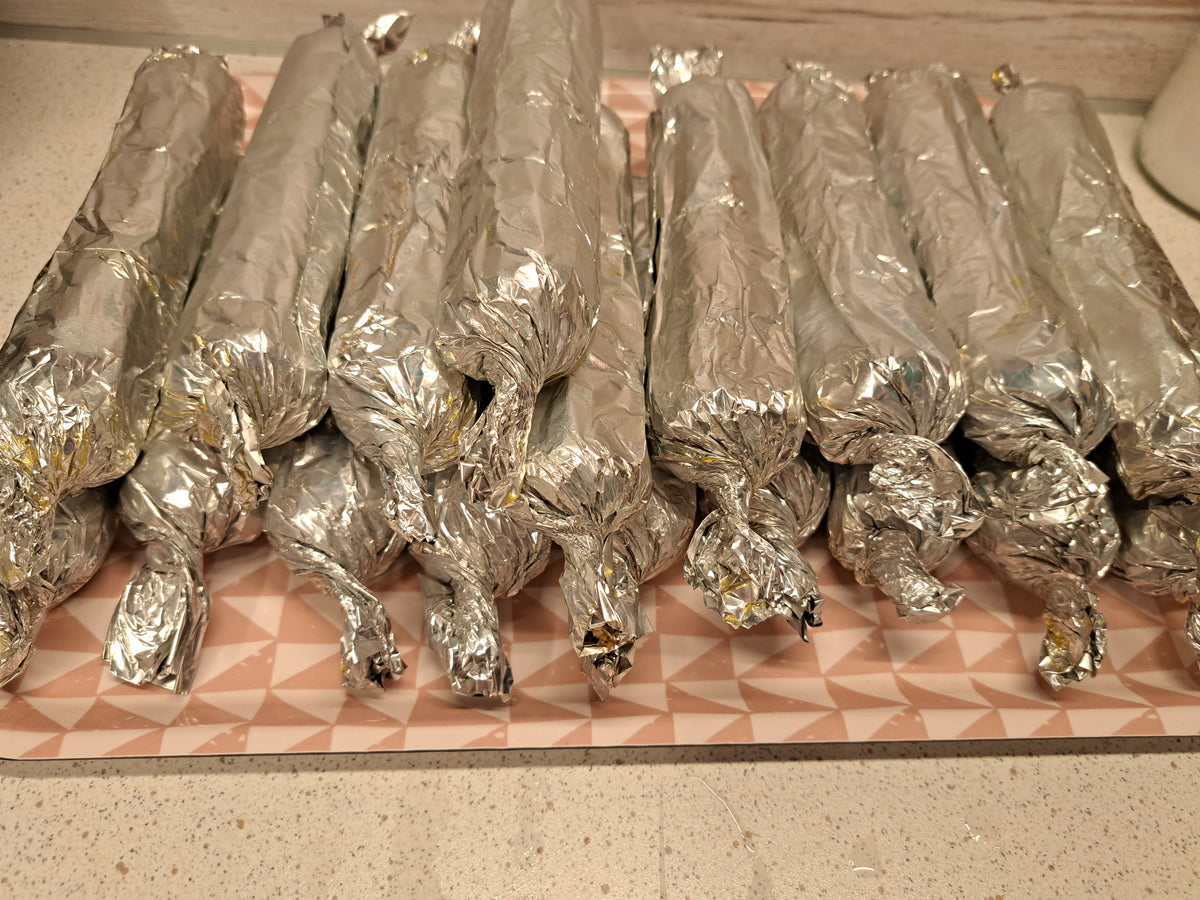 Freshly prepared embutido rolls wrapped in foil and arranged on a tray