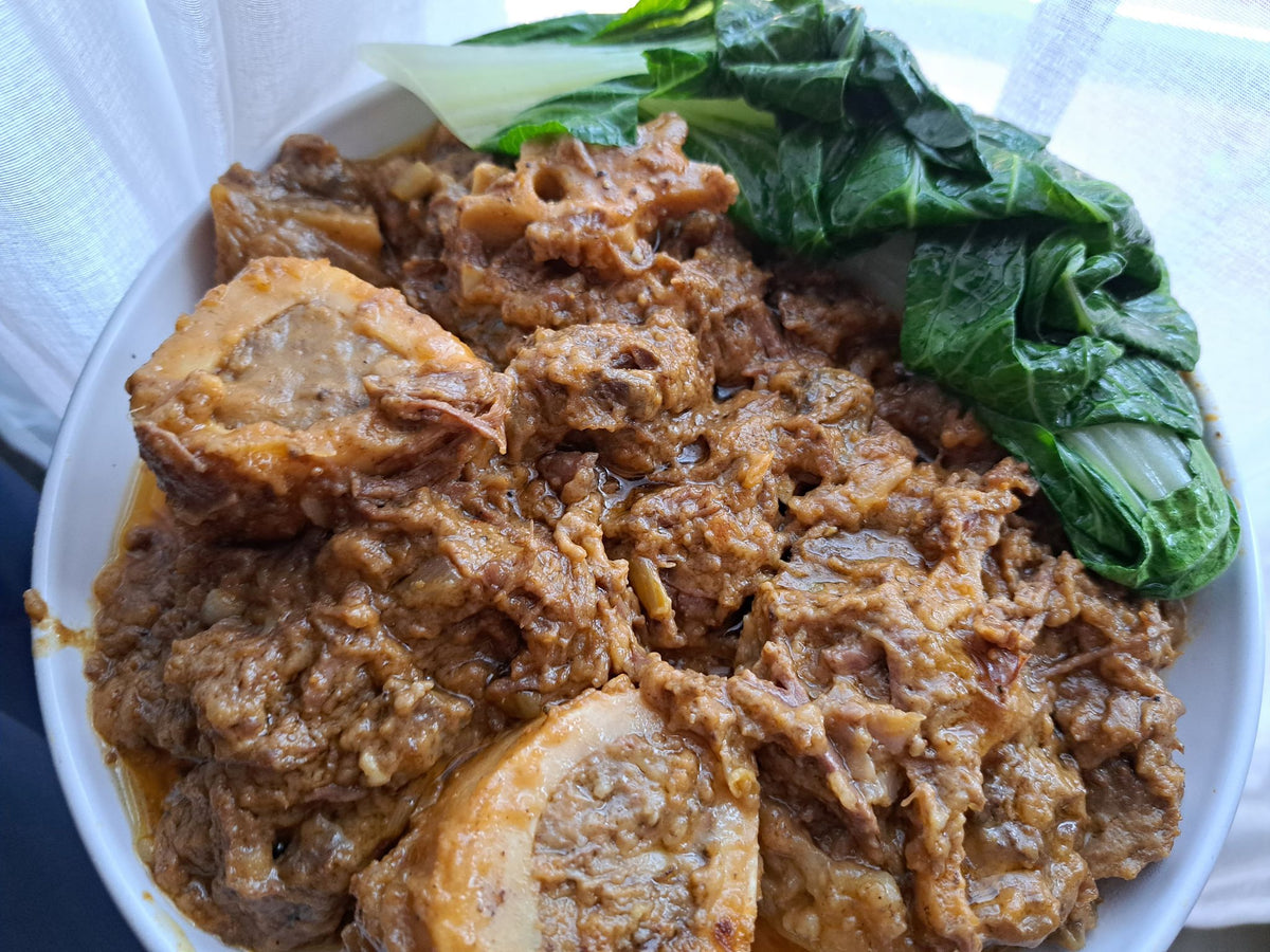 Beef kare-kare with marrow bones and bok choy in a serving bowl