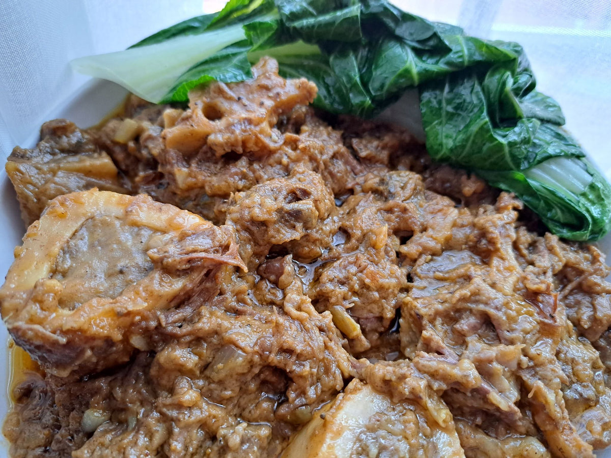 Close-up of beef kare-kare in rich peanut sauce with leafy greens