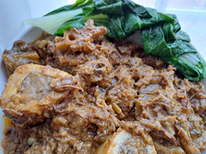 Close-up of beef kare-kare in rich peanut sauce with leafy greens
