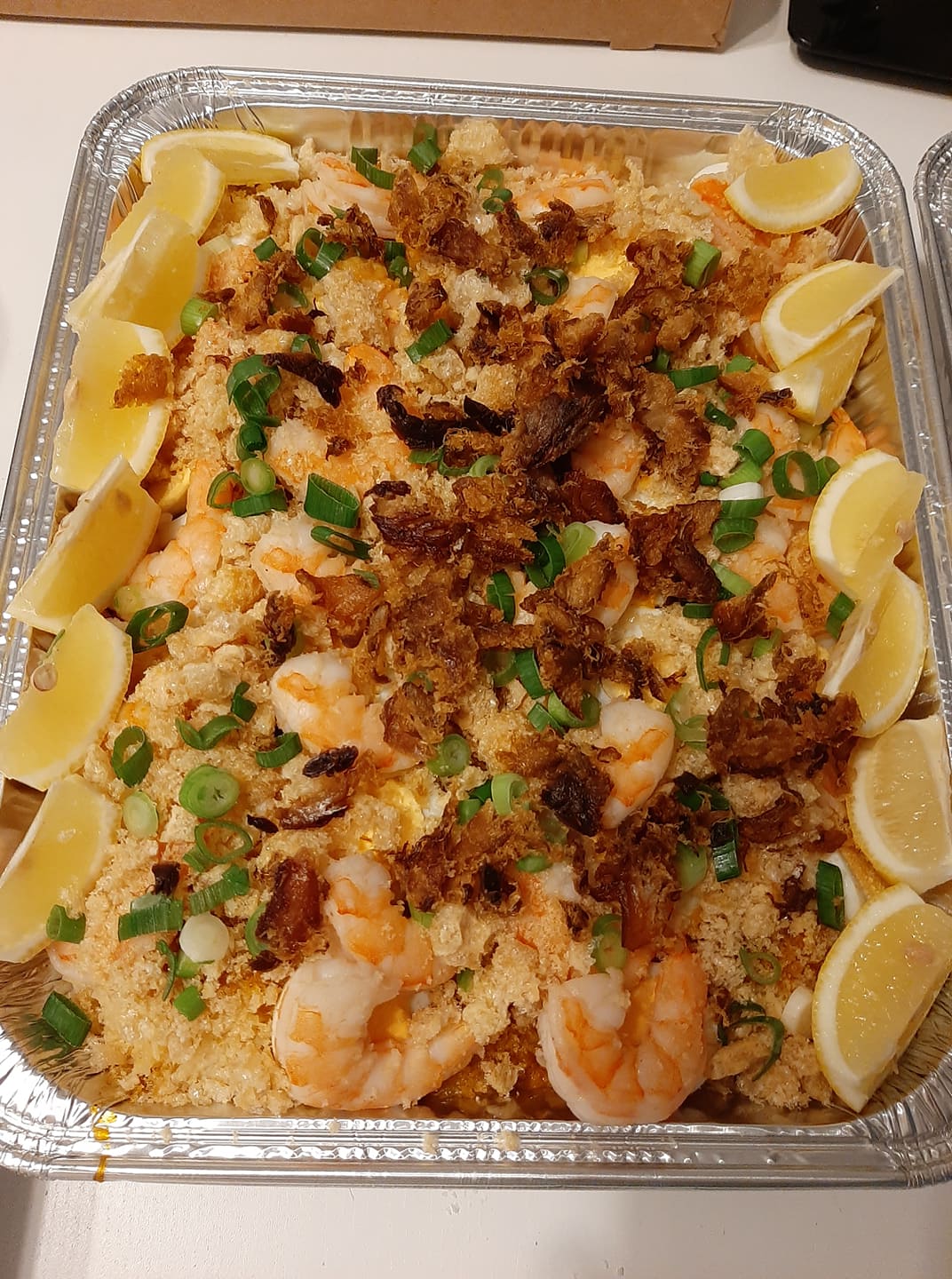 Full foil tray of pancit palabok topped with shrimp and chopped spring onions
