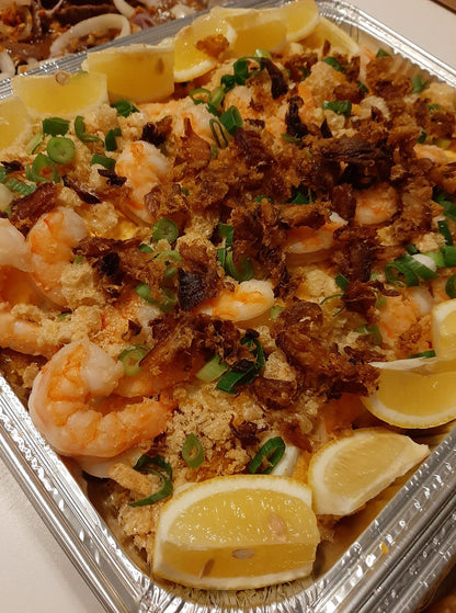 Angled close-up of pancit palabok with shrimp, lemon and crunchy garnish