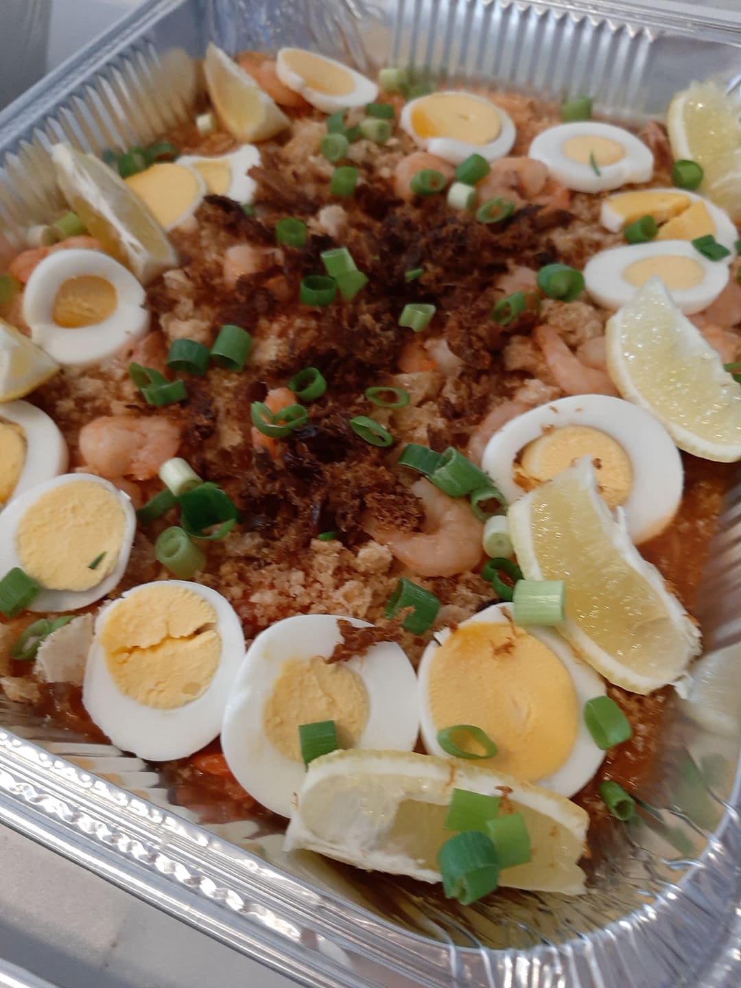 Overhead tray of pancit palabok decorated with eggs and lemon wedges