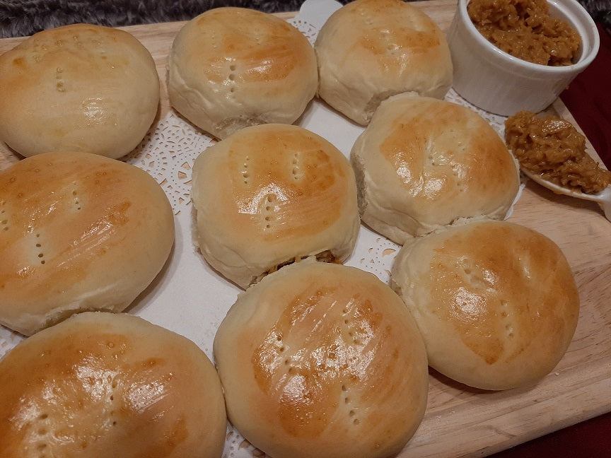 Glossy pan de coco rolls served on a board with coconut filling beside them