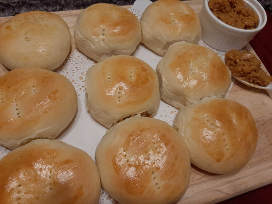 Glossy pan de coco rolls served on a board with coconut filling beside them
