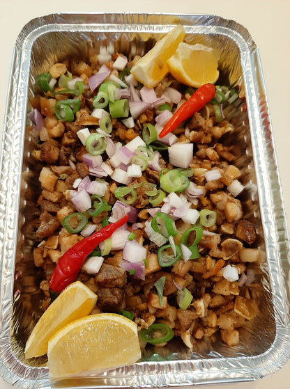 Pork sisig in a foil tray garnished with chillies, spring onions and lemon