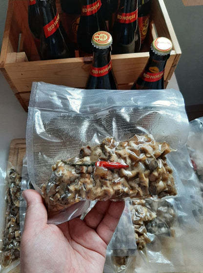 Hand holding a sealed pork sisig portion in front of bottled drinks